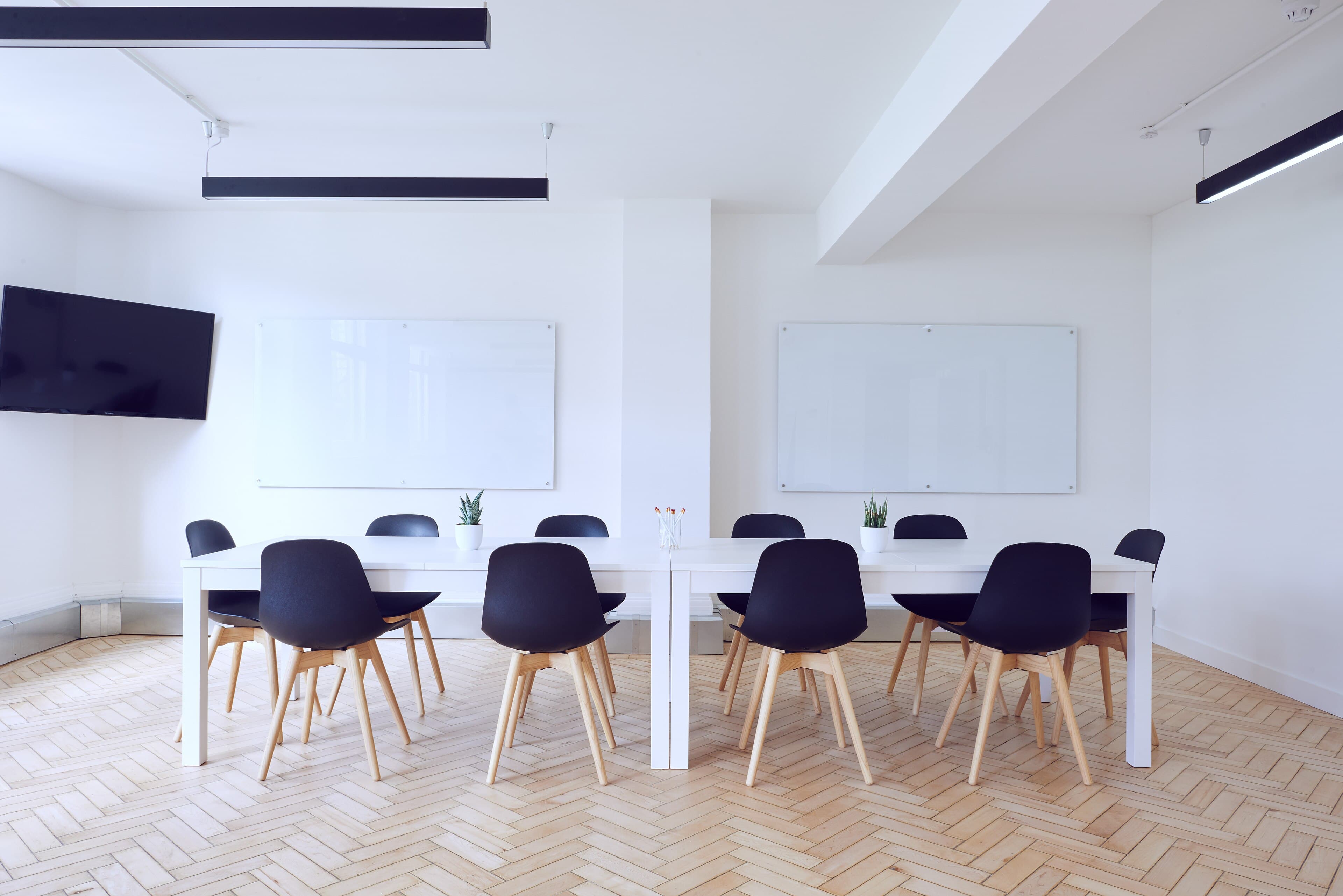 Bright meeting room with a long white table, whiteboards and black chairs